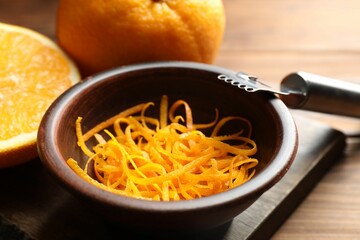 Orange zest, zester tool and fresh fruits on wooden table, closeup