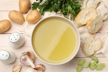 Tasty chicken bouillon in bowl, bread and ingredients on wooden table, flat lay