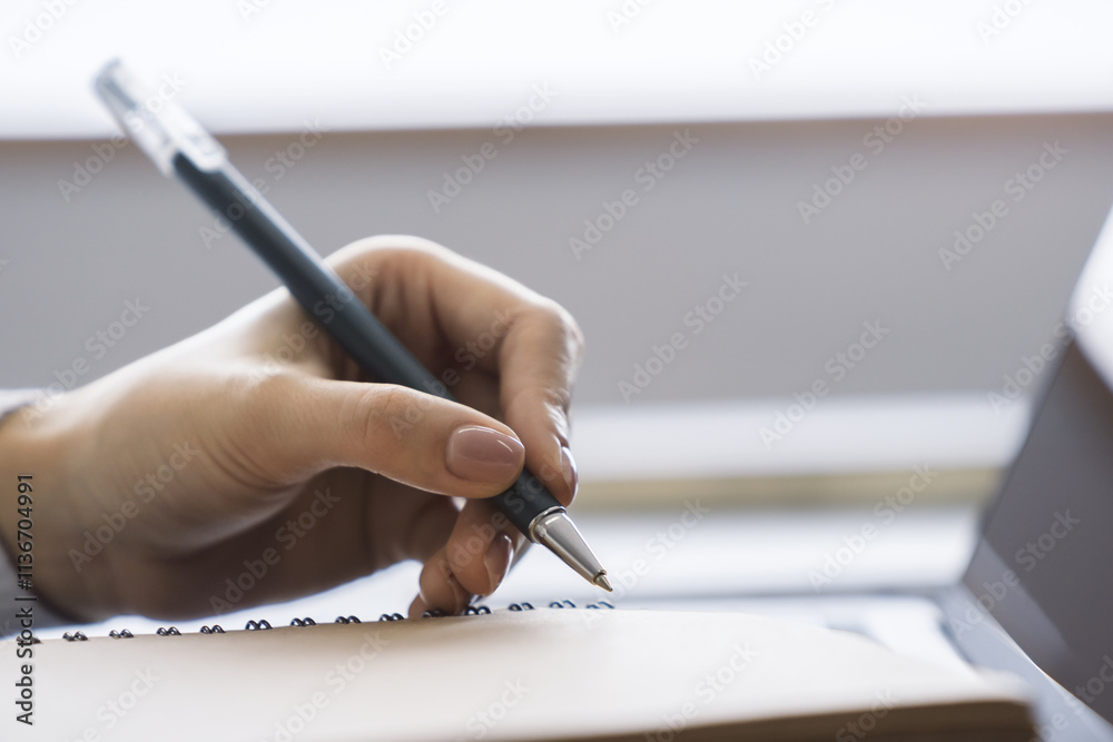 Poster the image focuses on a woman's hand scribbling in a notepad on a stylish laptop, set against a blurr