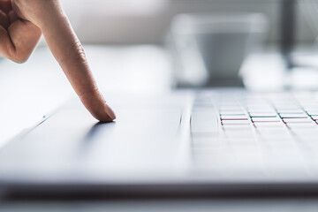 Close-up shot of a woman's hands typing on a modern laptop keyboard, with a blurry office scene...