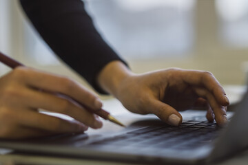 Female hands typing on a trendy laptop keyboard, with a blurry office scene in the background