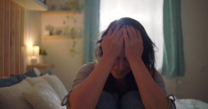 Woman sitting on bed, face buried in her arms, overwhelmed by sadness and isolation, themes of introspection, grief, and emotional pain