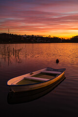 Naklejka premium Sunset over calm water with a small boat anchored at lakeside resort location