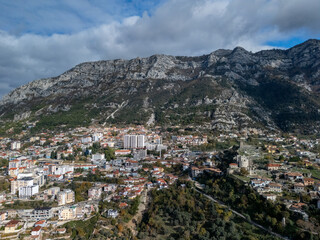 Obraz premium An aerial view of Kruje nestled against a rugged mountain range under a partly cloudy sky. Albania