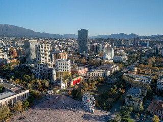 Aerial view of Tirana, Albania, showcasing modern architecture, Skanderbeg Square, and surrounding mountains under a clear blue sky.