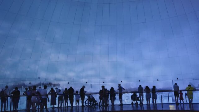 Silhouettes of people standing near a large aquarium exhibit with blue water reflections and a curved glass panel in the background