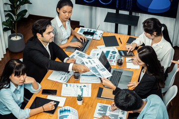 Wide top view of diverse group of business analyst team analyzing financial data report paper on meeting table. Chart and graph dashboard by business intelligence analysis. Meticulous