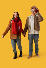 Young couple in winter clothes walking on yellow background