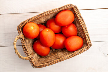 Fresh juicy tomatoes in a basket on a wooden table, close-up, top view.