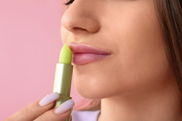 Young woman applying lip balm on pink background. Closeup
