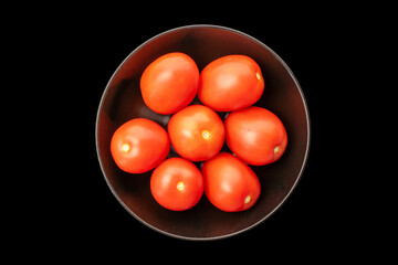 Fresh juicy tomatoes in a black ceramic plate on a black background, close-up, top view.