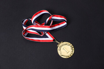 Golden medal with striped ribbon on black background, above view
