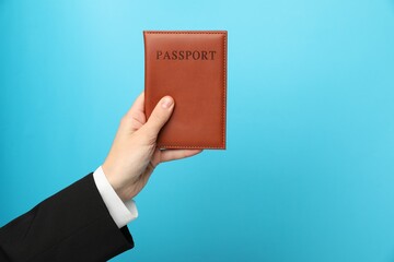 Woman holding passport in bright cover on light blue background, closeup. Space for text