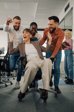 Business colleagues pushing businesswoman on office chair, having fun and celebrating success