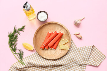 Wooden plate with tasty crab sticks, cut lemon, rosemary and bowl of salt on pink background © Pixel-Shot