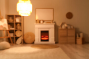 Blurred view of living room with fireplace, drawers and glowing lamp in evening