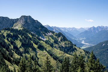 Berglandschaft mit bewaldeten Hängen und Tälern unter blauem Himmel