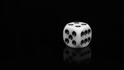 A close-up shot of a single white 6-sided die with black dots on a black background