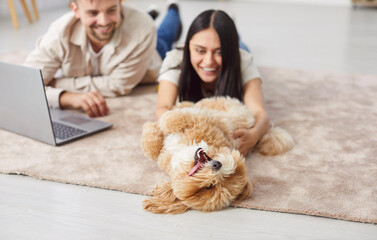 Family couple playing with dog at home, enjoying leisure time together. The pet owners interact with animal in a warm domestic environment, highlighting the bond between them and pet.