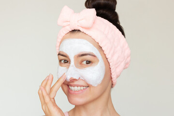Young pretty Caucasian brunette woman with a pink headband and a white mask on her face pampering...