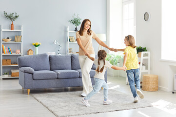 Funny mother dancing and playing with son and daughter at home. The family enjoys time together,...