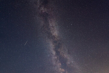A breathtaking view of the Milky Way galaxy stretching across the night sky, illuminated by countless stars. A meteor streaks across the scene.