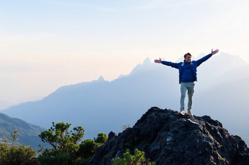 Obraz premium Triumphant Hiker Standing on Rock Summit Against Majestic Mountain Landscape