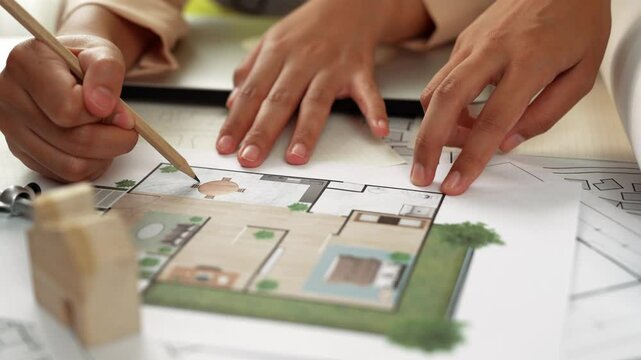 Professional engineer team discussion about house design on meeting table with architectural equipment and building blueprint scatter around at modern office. Focus on hand. Closeup. Delineation.