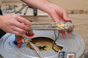 Repairman demonstrates a burnt-out boiler heating element covered with lime coating. Electric Water...
