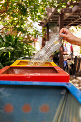 Une personne jette une bouteille plastique dans une poubelle de recyclage