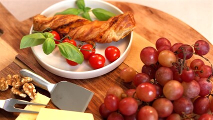 Rustic Mediterranean display with golden bread twist, deep red grapes, fresh basil, and ripe cherry tomatoes, celebrating seasonal ingredients in a warm, wholesome presentation.