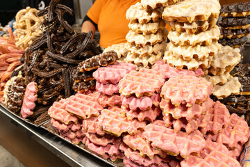 Close-up of a stack of chocolate-covered waffles and churros at a street market stall