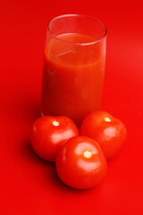 glass of tomato juice and tomatoes on red background
