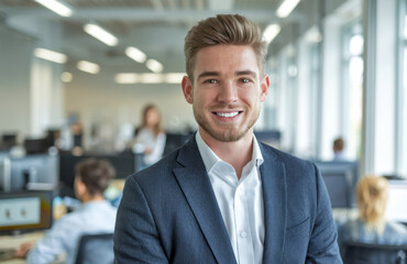 Fototapeta premium Cheerful young businessman with a formal outfit in a bright and open workspace, reflecting confidence and leadership, with colleagues working collaboratively in the background.