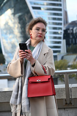A young woman of European appearance writes a message in a messenger on a smartphone against the backdrop of Moscow City skyscrapers