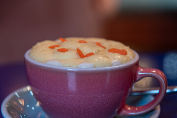 Close-up view of purple porcelain cup of pumpkin latte made from espresso, milk, whipped cream and caramel sprinkles standing on blue table in cafe or restaurant. Inspirational coffee drinks theme.