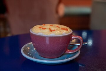 Close-up view of purple porcelain cup of pumpkin latte made from espresso, milk, whipped cream and caramel sprinkles standing on blue table in cafe or restaurant. Inspirational coffee drinks theme.