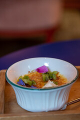 Close-up view of Crème brûlée (creme brulee, also known as burnt cream or Trinity cream) with kiwi and edible flowers in white bowl standing on wooden server. Soft focus. Copy space. Desserts theme.