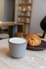 Close-up view of ceramic cup of white blank pumpkin latte made from espresso, milk and pumpkin puree with thyme standing by fresh croissant on table in coffeehouse. Soft focus. Copy space. Hot drinks.