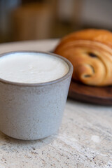 Close-up view of ceramic cup of white blank pumpkin latte made from espresso, milk and pumpkin puree with thyme standing by fresh croissant on table in coffeehouse. Soft focus. Copy space. Hot drinks.
