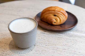 Close-up view of ceramic cup of white blank pumpkin latte made from espresso, milk and pumpkin puree with thyme standing by fresh croissant on table in coffeehouse. Soft focus. Copy space. Hot drinks.