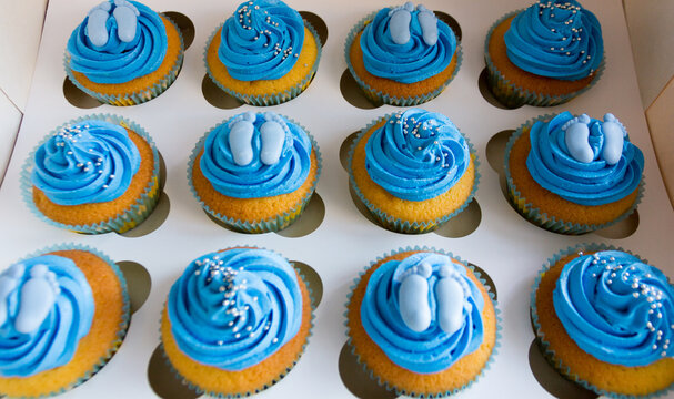 Close-up of a Box of cupcakes with blue buttercream icing and baby feet decorations in a cake box for a gender reveal party