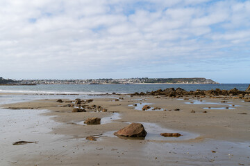 Depuis la plage de Trez Rouz, une vue paisible s’ouvre sur Camaret-sur-Mer à l’horizon, sous un ciel bleu avec de légers voiles nuageux.