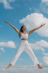 Obraz premium A woman in white pants and a white top is posing for a photo with her arms raised in the air. Concept of freedom and positivity, as the woman is enjoying herself and embracing the moment