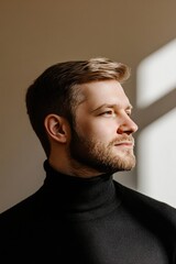 Thoughtful Young Man in Black Turtleneck Standing in Sunlit Interior