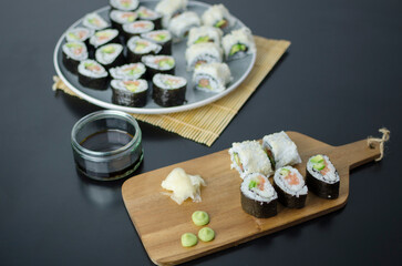 Homemade sushi rolls with salmon and avocado on a wooden board and grey plate, sushi selection, on a black backgroun