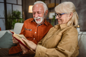 senior couple husband and wife sit on sofa and read a book together