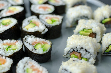 Homemade sushi rolls with salmon and avocado on a wooden board and grey plate, sushi selection, soy sauce, on a black background, top view