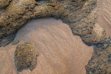 Smooth untouched fine sand and rough sandy rocks on a beach on a sunny day, viewed from above....
