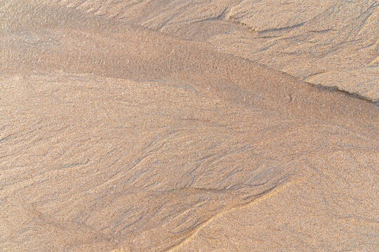 Abstract shapes and patterns in the grainy sand and flowing water on the beach on a sunny day, viewed from above. Abstract textured natural sandy background, top view. Copy space.